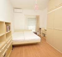 A bedroom in a 2-room apartment with a bed, shelves, and air conditioning.