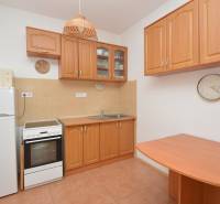 A kitchen in a 2-room apartment with wooden furniture, appliances, and ceramic tiles.