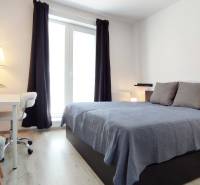 Bright bedroom in a 2-room apartment with a bed, table, and window with curtains.