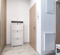A hallway with white furniture and coat hooks in a 2-room apartment, light wooden floors.