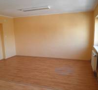 An empty office with wooden flooring and yellow walls, illuminated by daylight.