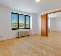 A spacious room with a wooden floor, a large window, and wooden doors in a family house.