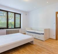 A bright room with a wooden floor, a bed, and a window overlooking the garden in a family house.