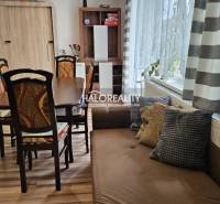 Dining room in a family house with a wooden table, chairs, and a sofa, light curtains.