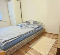 A bedroom in a family house, simply furnished with a bed, a cabinet, and a wooden floor.