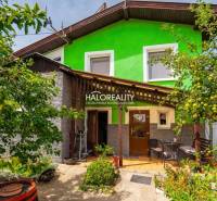 A family house in Banská Štiavnica with a wooden veranda, surrounded by greenery and fruit trees.
