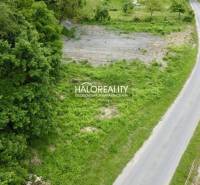 Residential plots in Selce by the road, bordered by greenery and a stream.