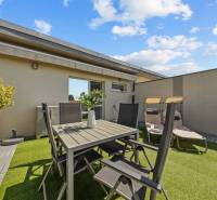 Terrace of a 4-room apartment with a table and chairs, surrounded by plants and loungers.