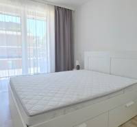 Bright bedroom with a large window, bed, and nightstand in a 2-room apartment.