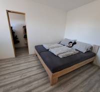 A bedroom in a family house with a bed, burgundy floor, and an entrance to the pantry.