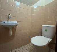 A toilet with a sink in a family house, tiled with beige tiles.