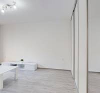 A bright living space in a two-room apartment with simple furnishings and large windows.