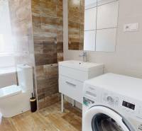 Bathroom in a 2-room apartment with a bathtub, washing machine, and wooden-style tiles.