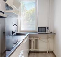 A kitchen with white cabinets, a sink, and a microwave in a 2-room apartment.