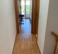 The hallway of the family house leads to a room with a bed and a desk.