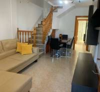 Living room of a family house with a beige sofa, dining table, and wooden staircase.