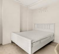 A bright bedroom with a white bed and a lamp in a 3-room apartment.
