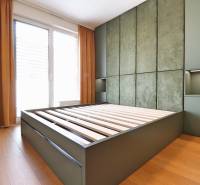 A bedroom in a two-room apartment with a bed and large windows with orange curtains.