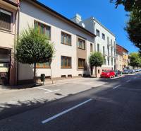 A street in Piešťany with apartment buildings and parked cars.