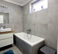 A bathroom in a family house with a bathtub, a sink, and gray tiles.