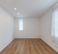 A room in a family house, white walls, wooden floor, a sash window with a light curtain.