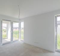 A spacious room with large windows and a raw floor in a family house.