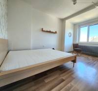 Bedroom in a 2-room apartment with wooden flooring, a bed, and a chair.