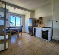 A kitchen in a 2-room apartment with a dining table, appliances, and a large window.