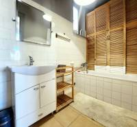 A bathroom in a 2-room apartment with a bathtub, a sink, and a wooden cabinet.