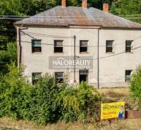 A two-story building in Hodruša - Hámre surrounded by greenery, with a real estate banner on the fence.