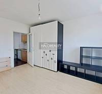 Studio apartment with white furniture, opening into a small kitchen; empty space, bright walls.