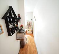 A narrow hallway with a wooden floor, shelves, and a small refrigerator in a two-room apartment.