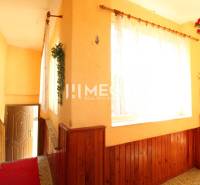 The hallway of a family house with a staircase, wooden paneling, and curtains on the windows.