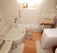 A bathroom in a family house with a bathtub, a washing machine, and a wall covered with tiles.