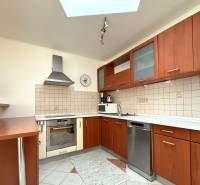 A kitchen in a family house with wooden cabinets, a dishwasher, and ceramic tiles on the wall.