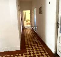 A hallway in a family house with tiles leading to a room with furniture.