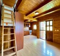 Interior of a family house with wooden walls, flooring, kitchen unit, and stairs to the upper floor.