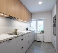 A kitchen in a studio apartment with modern equipment, light cabinets, and a large window.