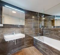 A bathroom in a 4-room apartment with a bathtub, sink, and washing machine, wooden and stone tiles.