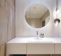 A bathroom in a 3-room apartment with a round mirror, light tiling, and a modern sink.