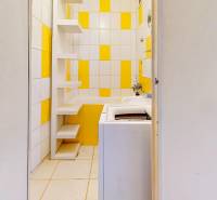 A bathroom with a washing machine and shelves in yellow and white tones in a studio apartment.