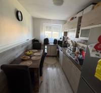 A kitchen in a 3-room apartment with a dining table, wooden floor, and a window.