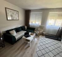 A bright living room in a three-room apartment with a sofa, an armchair, and a table on a light floor.
