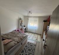 Bedroom with a bed and a bookshelf in a 3-room apartment, light flooring, decorative carpet.