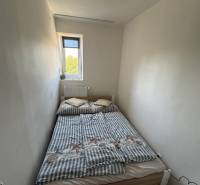 A small bedroom with a narrow window and a bed in a three-room apartment.