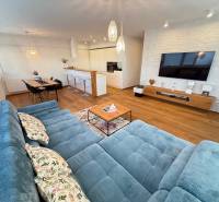 A spacious living room of a 4-room apartment with a comfortable couch and a TV on the wall.