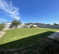 A garden of a family house in Prešov with a lawn, trees, and a terrace under a blue sky.