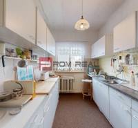 A kitchen in a family house with white cabinets, appliances, and a window with a white curtain.