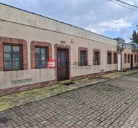 Partizanska Street in Svätý Jur with commercial spaces, brick windows and doors, paved sidewalk.