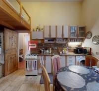 A kitchen in a 2-room apartment with a wooden gallery, dining table, and cabinets.